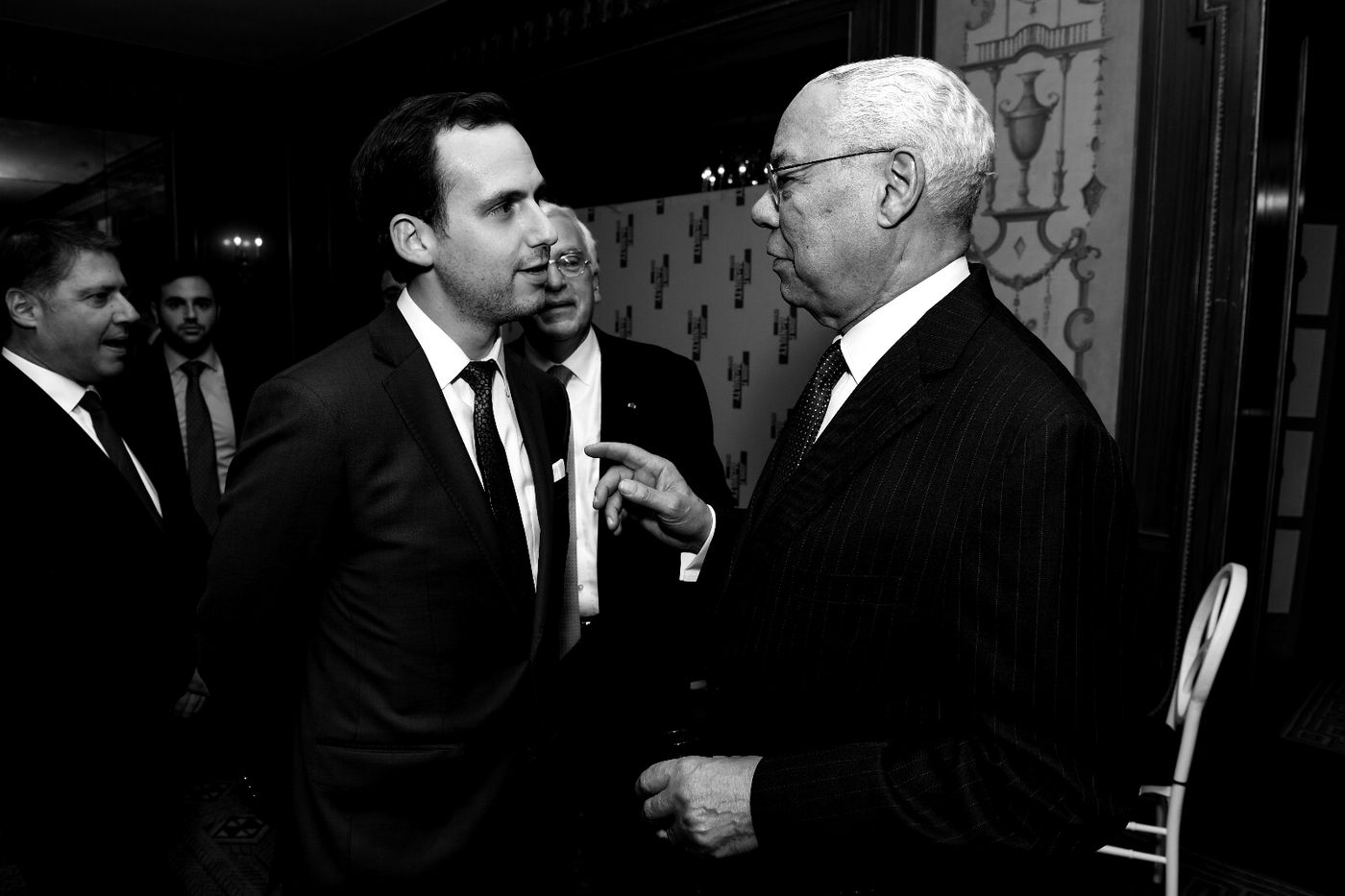 A younger man in conversation with a senior statesman at a reception